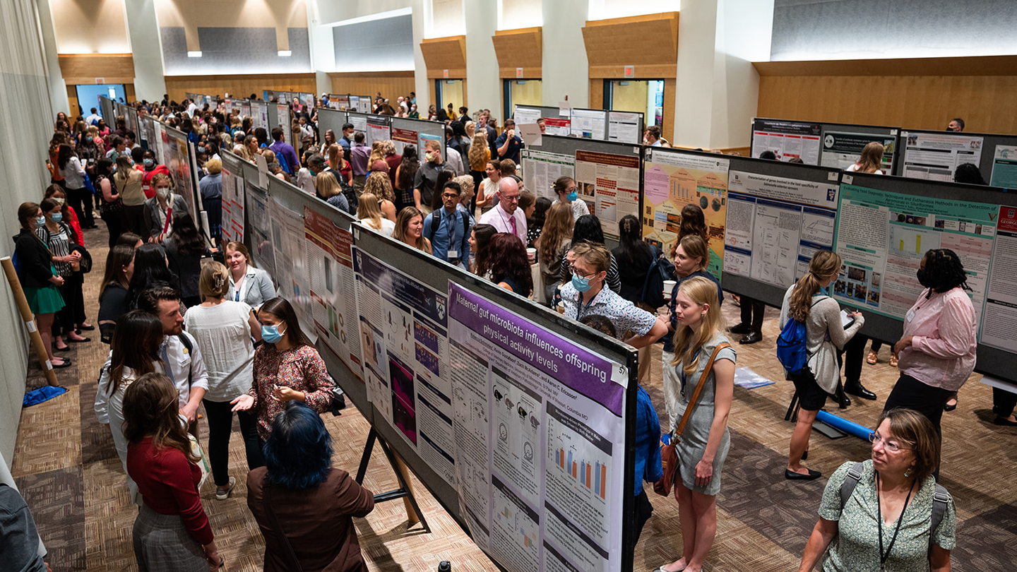 Photo of a big room with many people inside standing around serval poster 