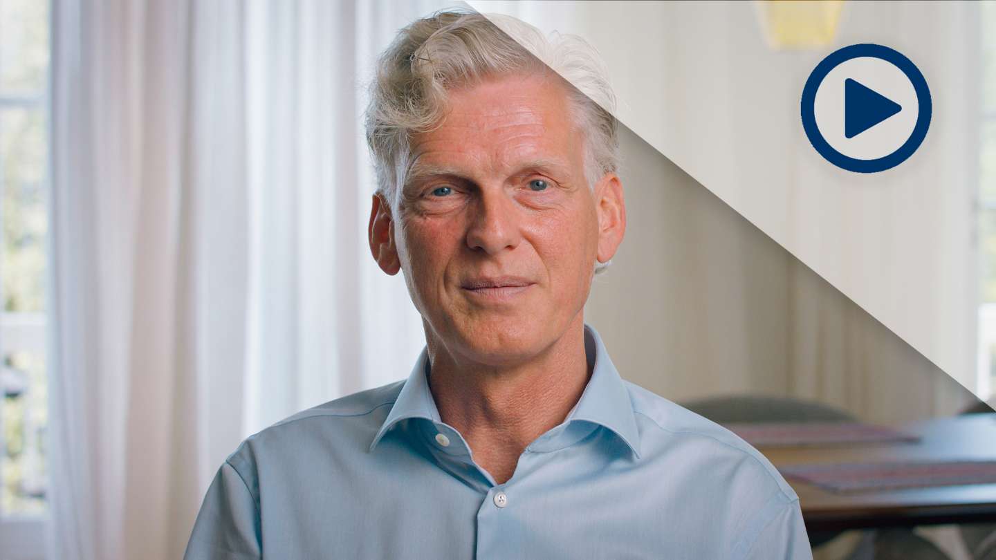 Headshot of white male in blue dress shirt sitting in living room and looking straight at the camera.